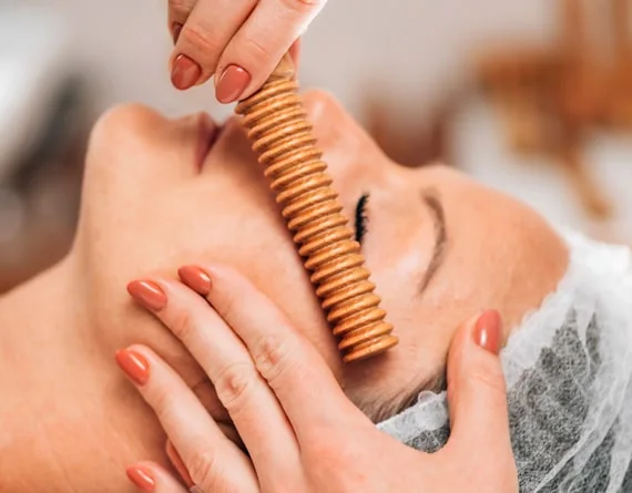 A small wooden massage roller along the cheek during facial care.