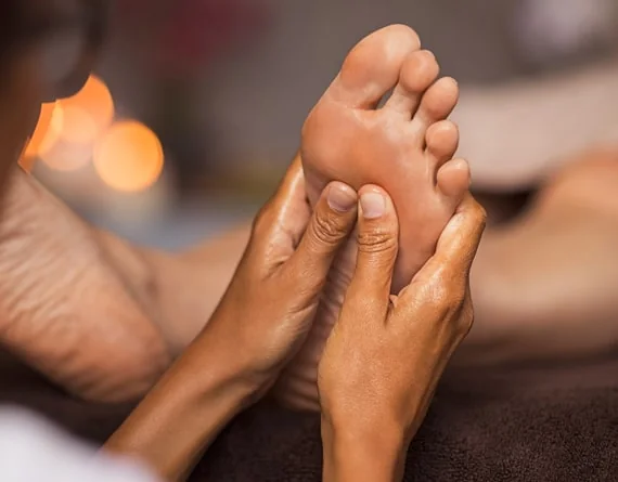 Ruke terapeuta koje masiraju taban i područje prstiju stopala.